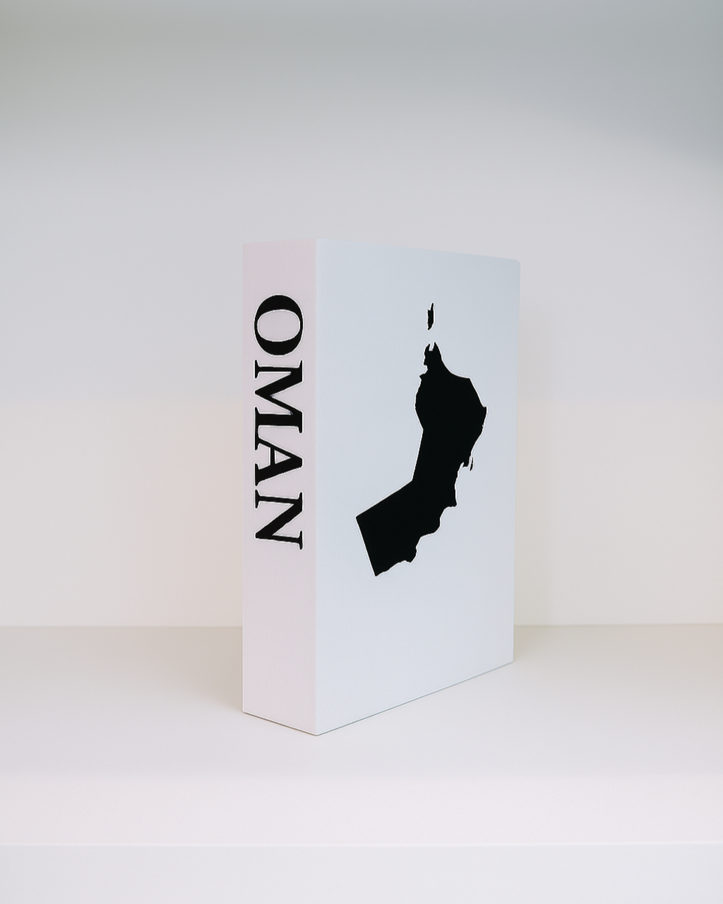 White book with black silhouette of Oman and 'Oman' text on a white background